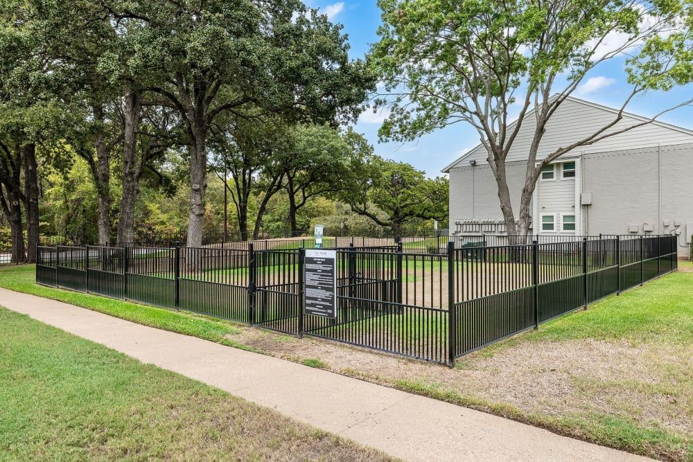 a dog park with a fence and trees in front of a house at The Park at Flower Mound in Flower Mound, TX..