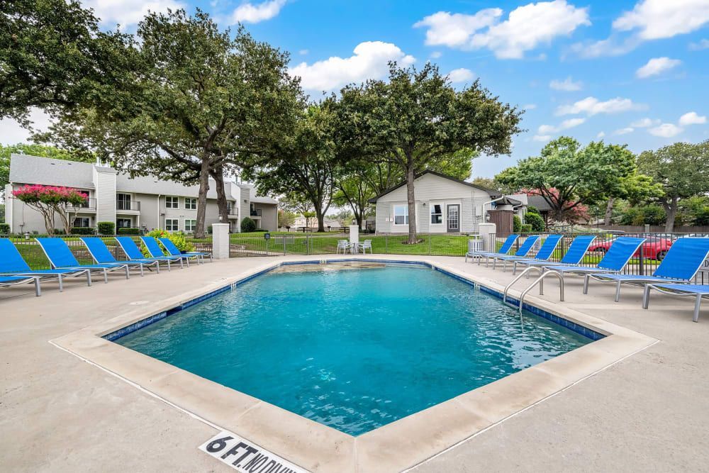 a large swimming pool is surrounded by blue chairs and trees at The Park at Flower Mound in Flower Mound, TX.