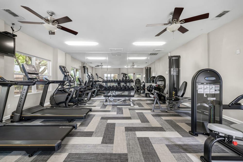 a large gym with treadmills , dumbbells , and a ceiling fan at The Park at Flower Mound in Flower Mound, TX.