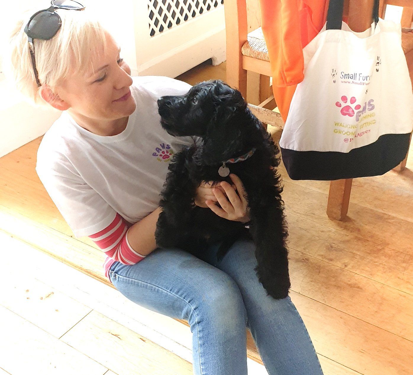 Middle aged woman in jeans holding a small black puppy.