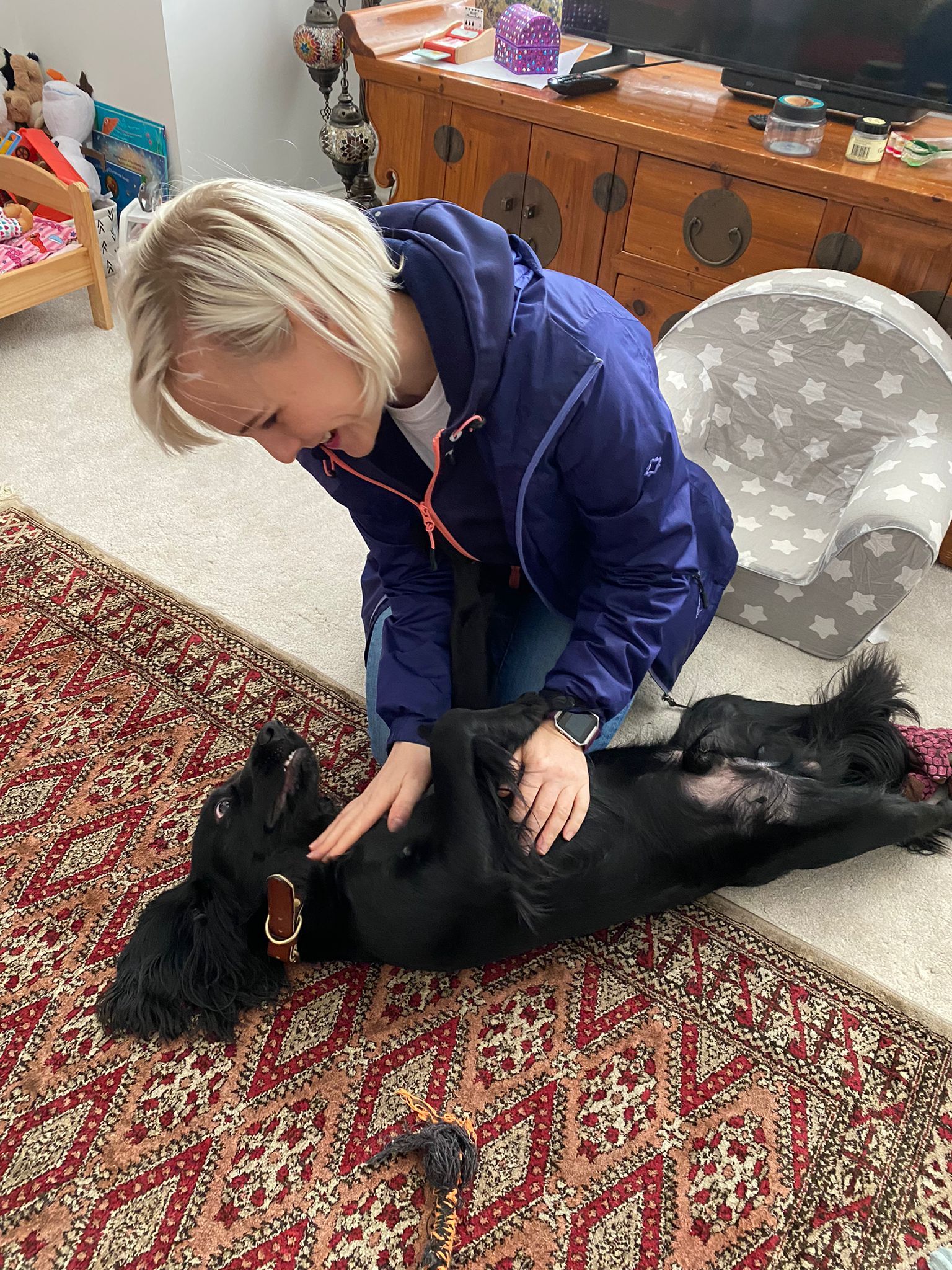 Middle-aged woman fussing a small black dog after belly rubs.