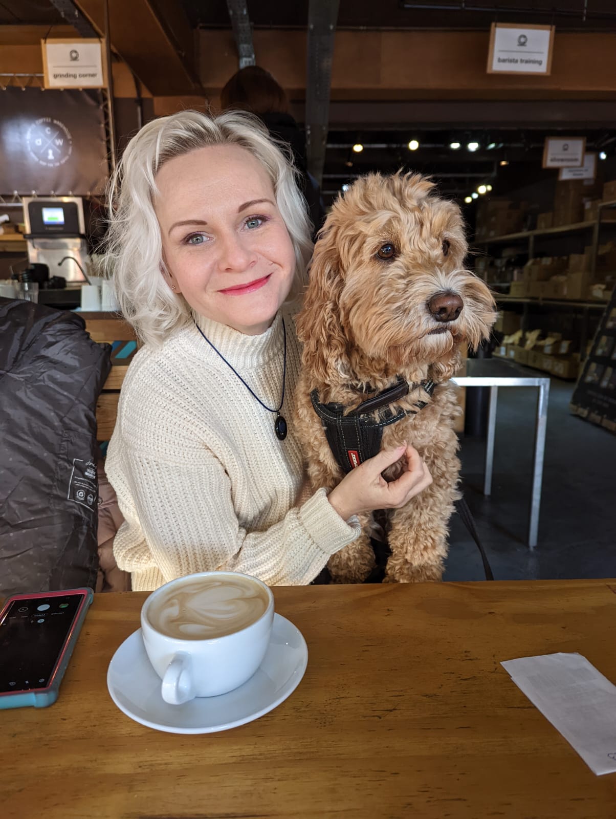 A middle-aged woman having coffee, cuddling a fluffy middle-sized dog on her lap.