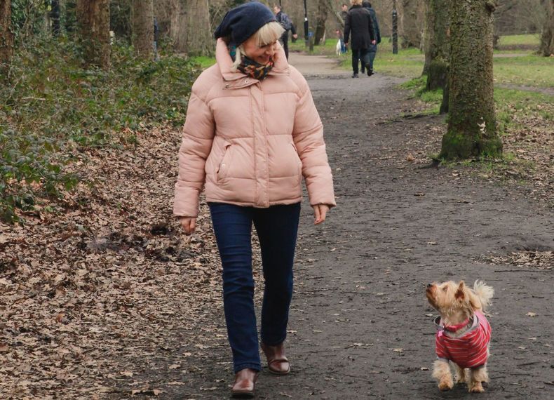 A woman in puffer jacket smiling down at the small dog walking beside her.