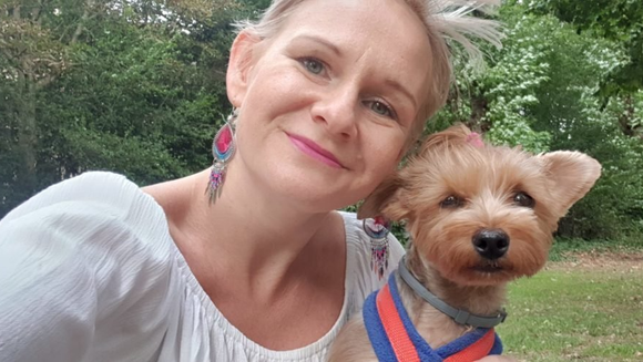 A middle-aged woman smiling at the camera, her small dog peering at the camera beside her.