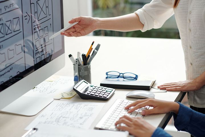 Una mujer señala una pantalla de computadora mientras un hombre escribe en un teclado.