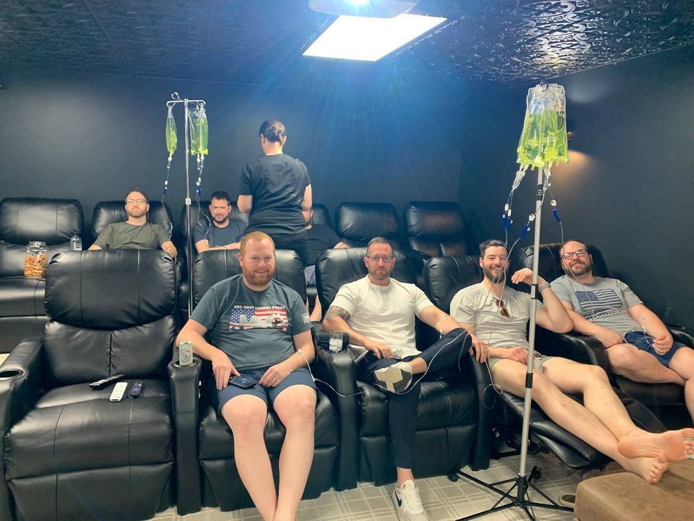 A group of men are sitting in chairs with iv drips in them.