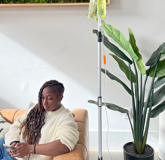 A woman is sitting on a couch with an iv in her arm.