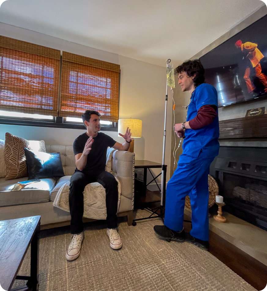 A man is sitting on a couch talking to a nurse in a living room.