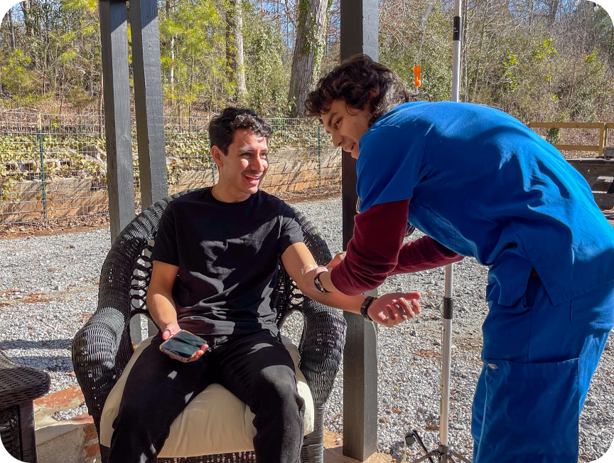 A man in a black shirt is sitting in a chair while a man in a blue shirt is standing next to him.