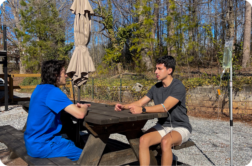 Two men are sitting at a picnic table talking to each other.