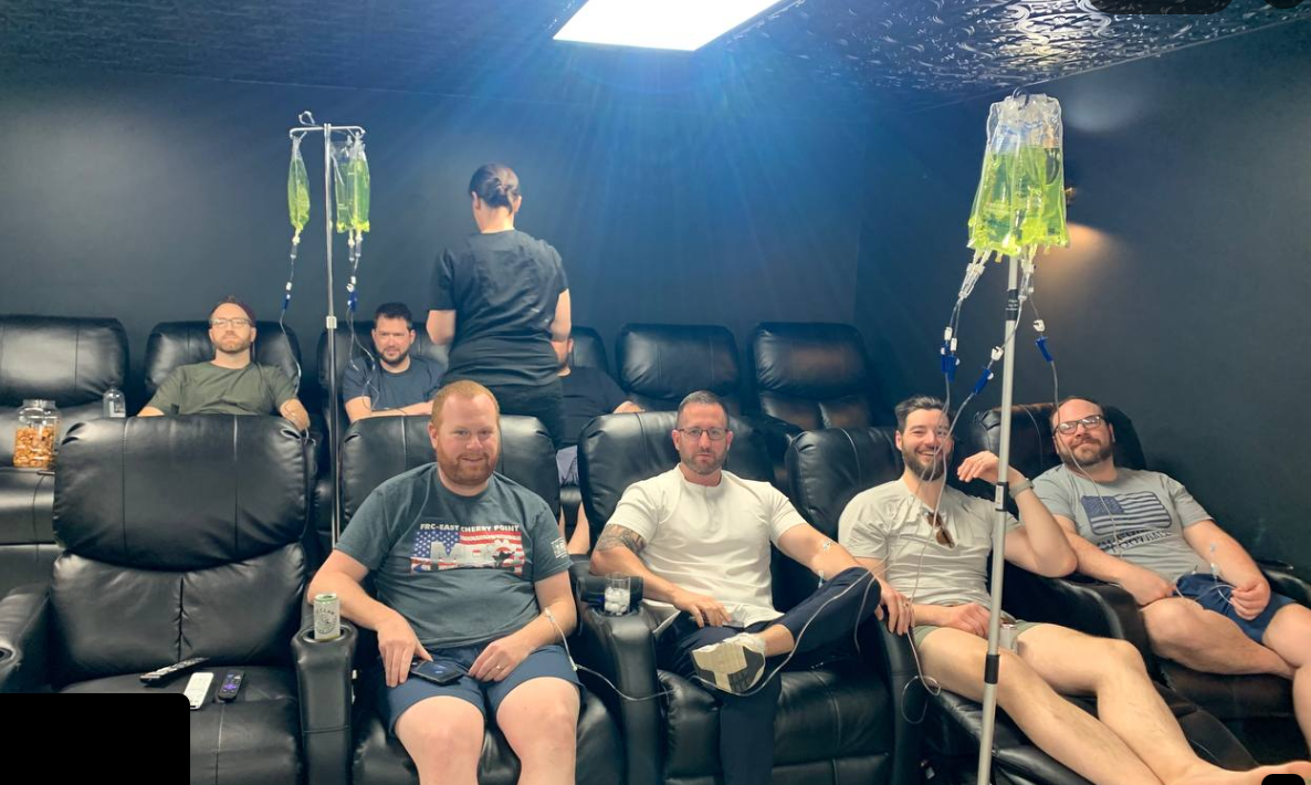 A group of men are sitting in chairs with iv drips in them.