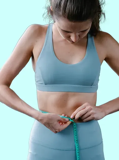 A woman is measuring her waist with a tape measure.