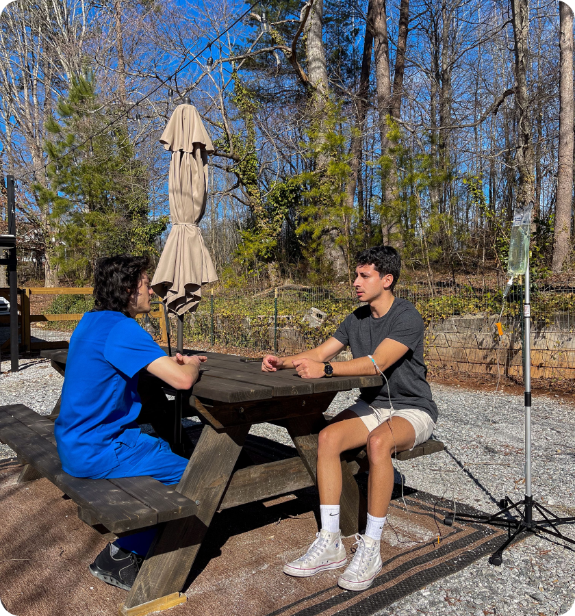 Two men are sitting at a picnic table talking to each other.