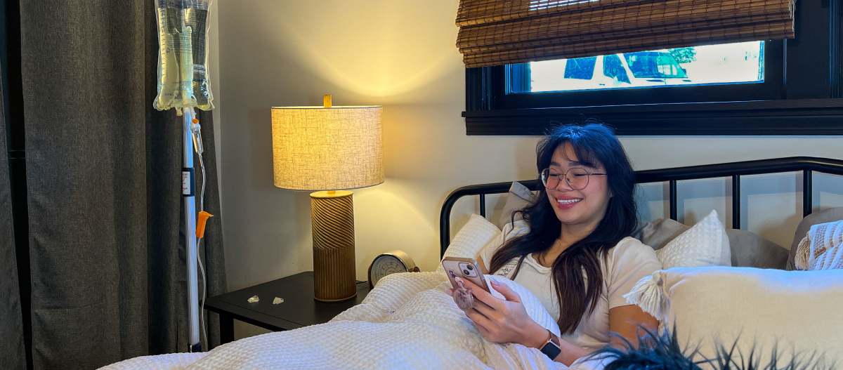 A woman is laying in bed with an iv in her arm and looking at her phone.