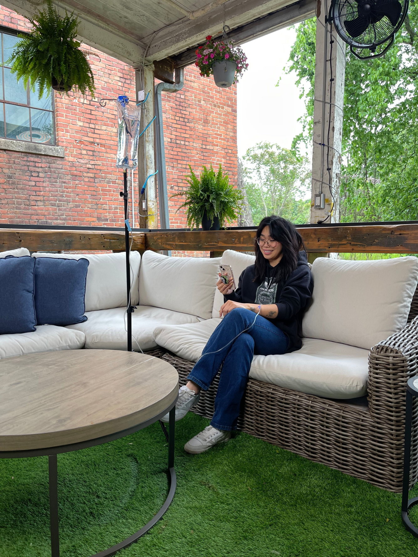 A woman is sitting on a couch on a porch looking at her phone.