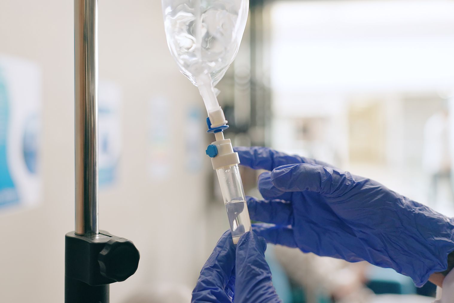A healthcare worker in blue gloves adjusts the drip chamber of an intravenous (IV) setup.
