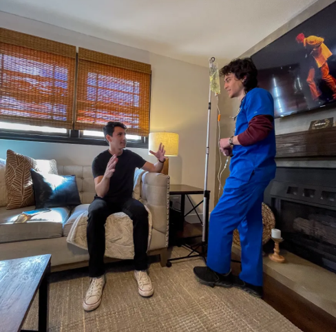 A man is sitting on a couch talking to a nurse in a living room.