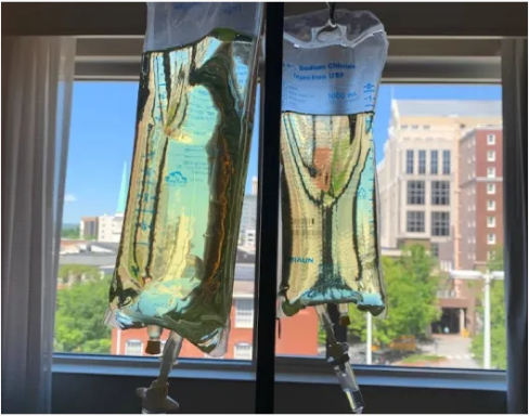 Two bags of liquid are hanging from a window in a hospital room.