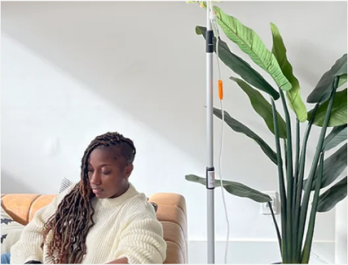 A woman is sitting on a couch with an iv in her arm.