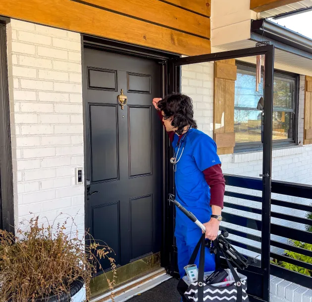 A man in a blue scrub suit is standing in front of a black door