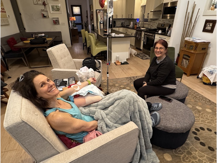 A man in a black shirt is sitting in a chair while a man in a blue shirt is standing next to him.