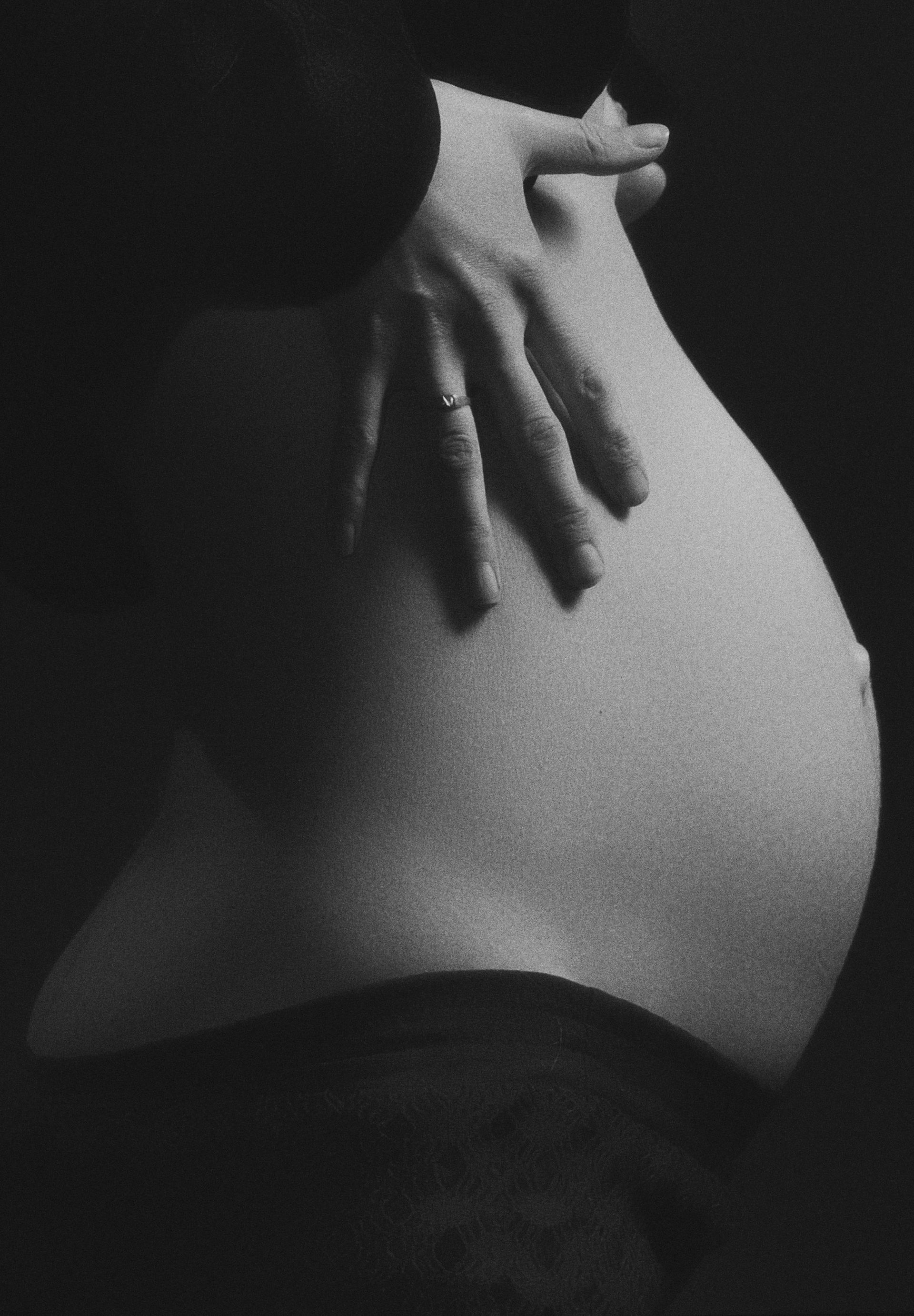 Pregnant belly, hand resting gently on the curved surface, black and white.