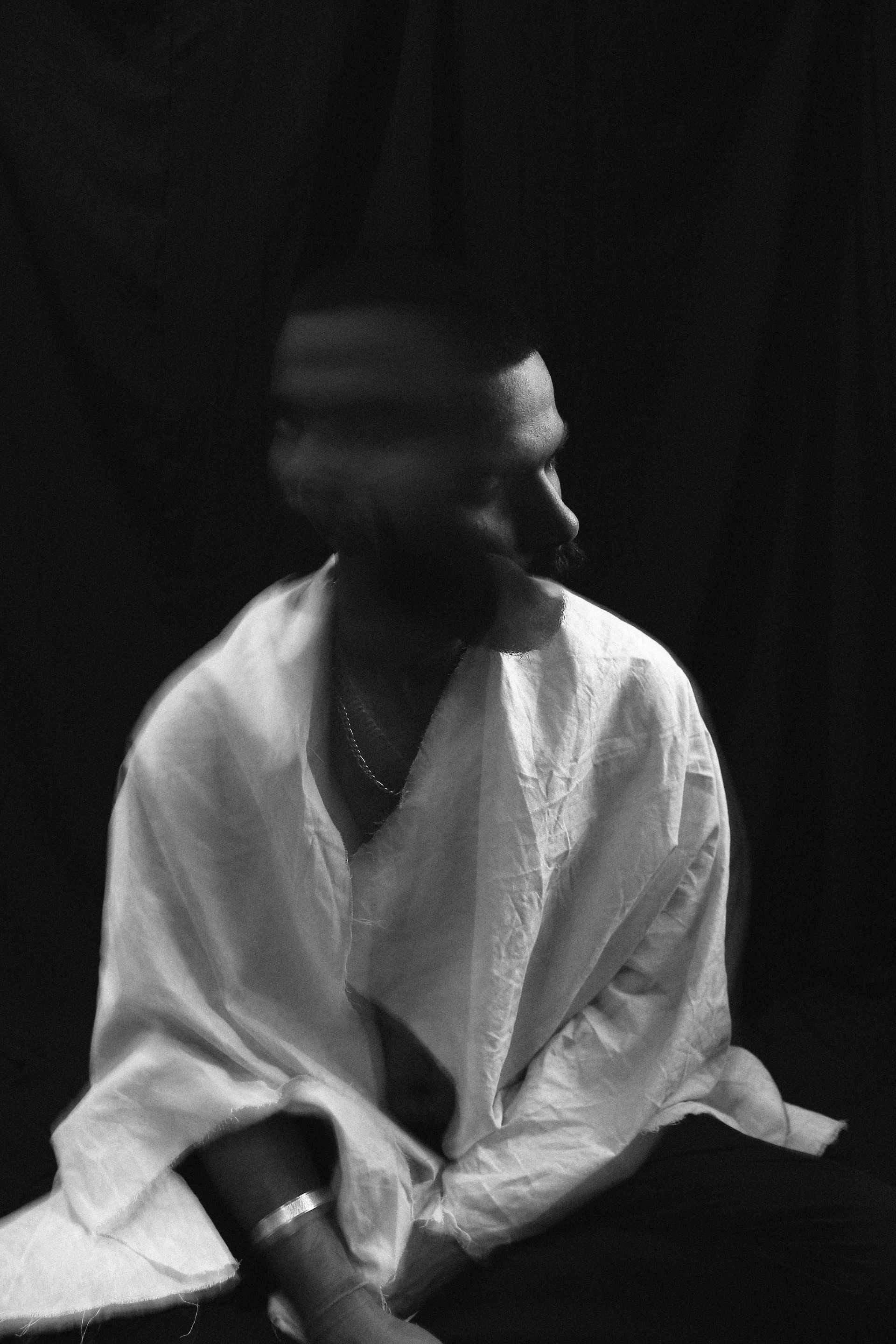 Black and white photo of a person in a white shirt, their head blurred, turned to the side against a dark background.