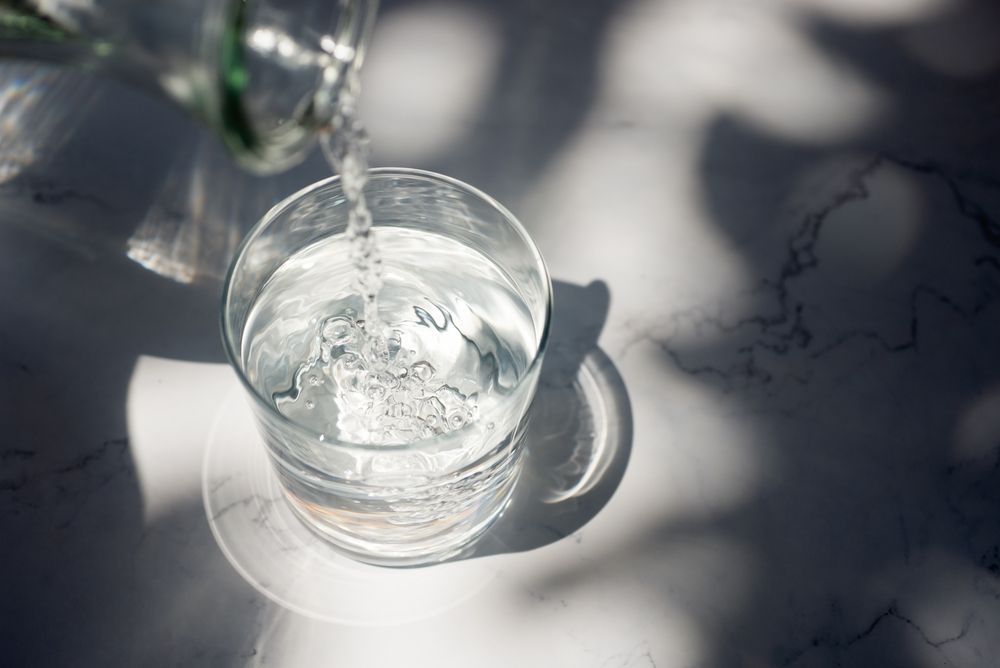 A glass of water is being poured into a glass on a table.