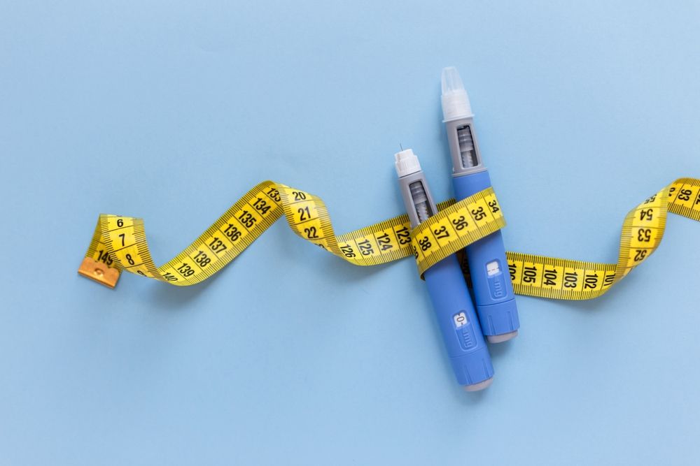 A pair of semaglutide pens wrapped in a measuring tape on a blue background.