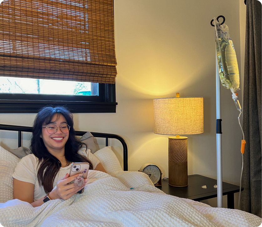 A woman is laying in bed with an iv in her arm and looking at her phone.