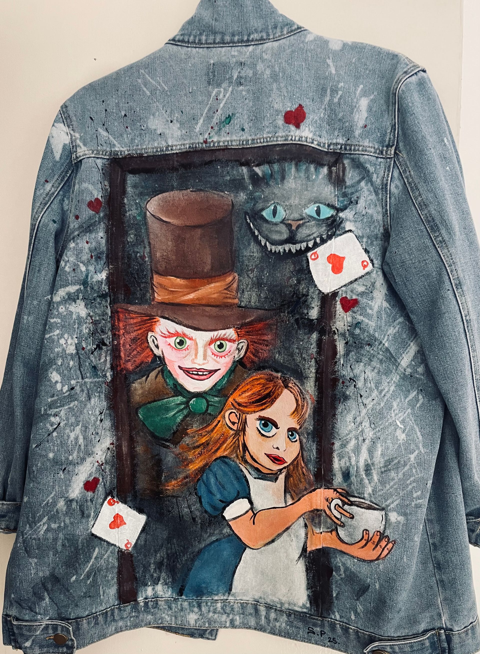 A denim jacket with a painting of Alice in wonderland, and the Mad Hatter