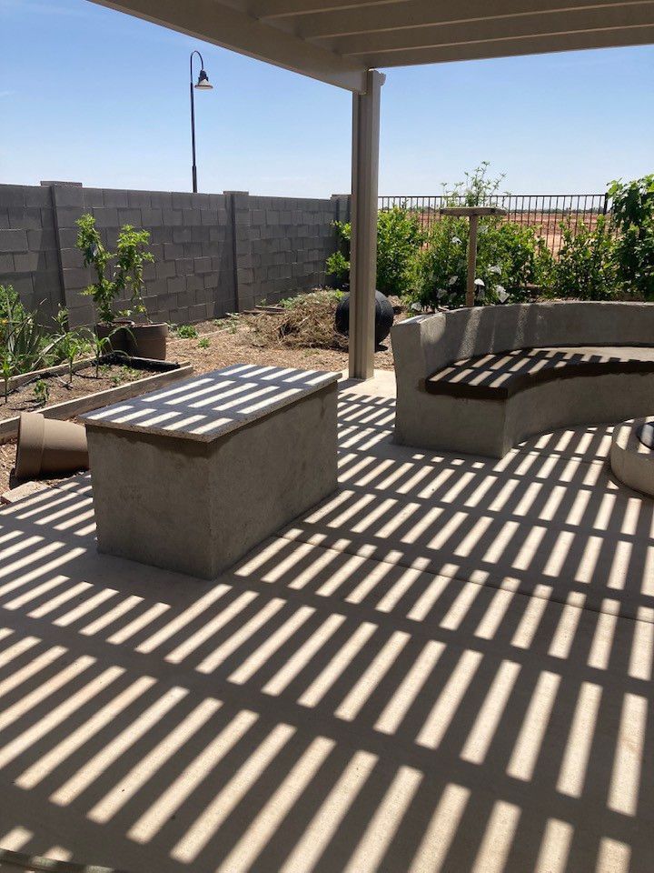 Concrete patio with pergola, table, bench casting shadow in sunny backyard.