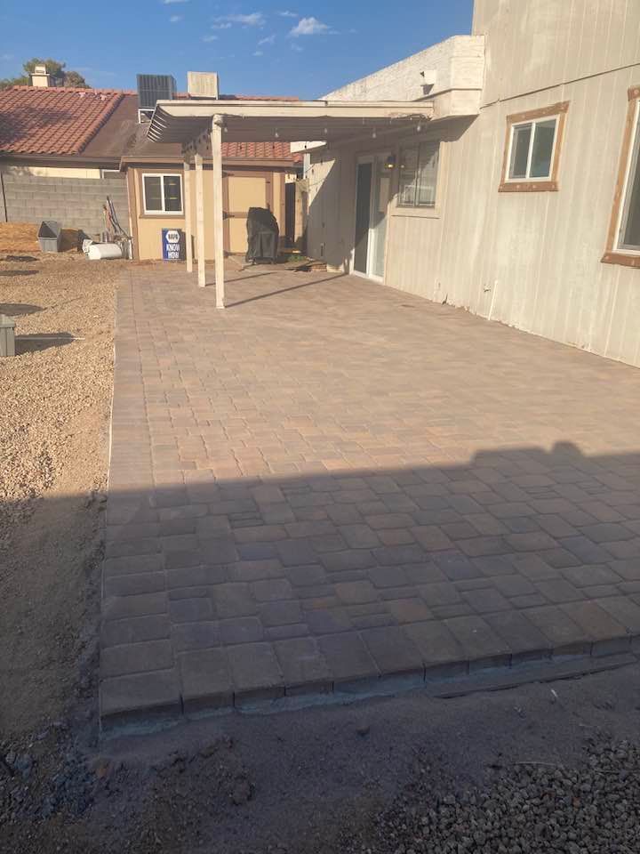 A newly paved brick patio with a small shed and pergola attached to the side of a house.