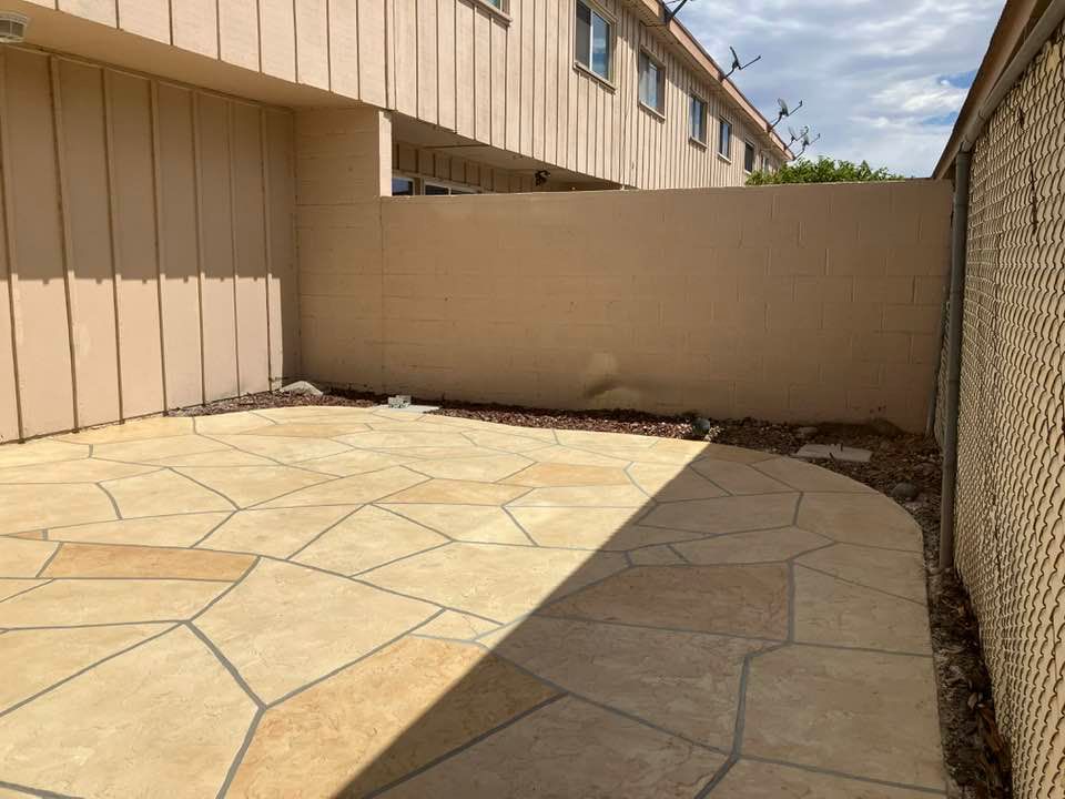 Patio with beige flagstone, tan walls, and a chain-link fence under a partly cloudy sky.