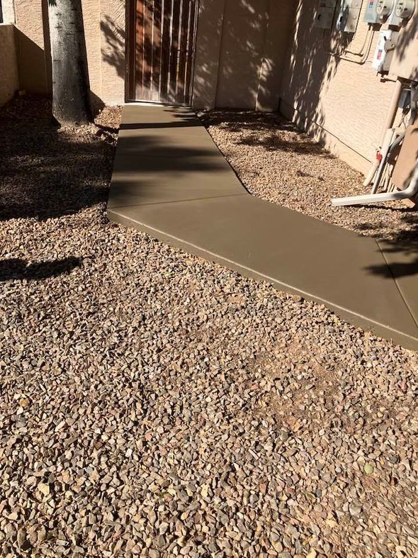 A new concrete pathway leading to a building entrance, surrounded by gravel.