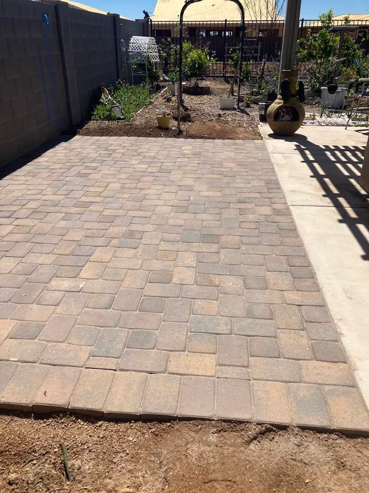 A paved patio in a backyard with a garden and fence.