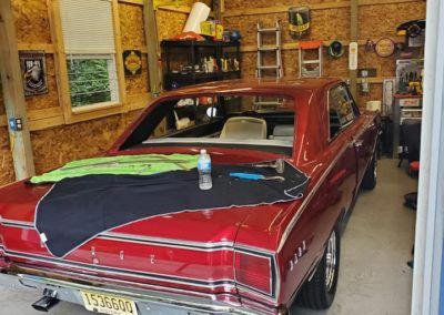 A red car is parked in a garage with a bottle of water on the floor.