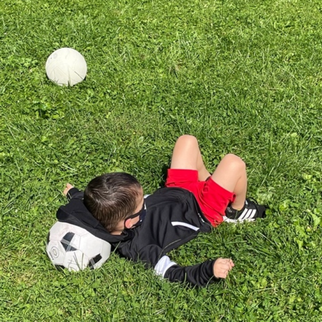 A young boy is laying on the grass with a soccer ball.