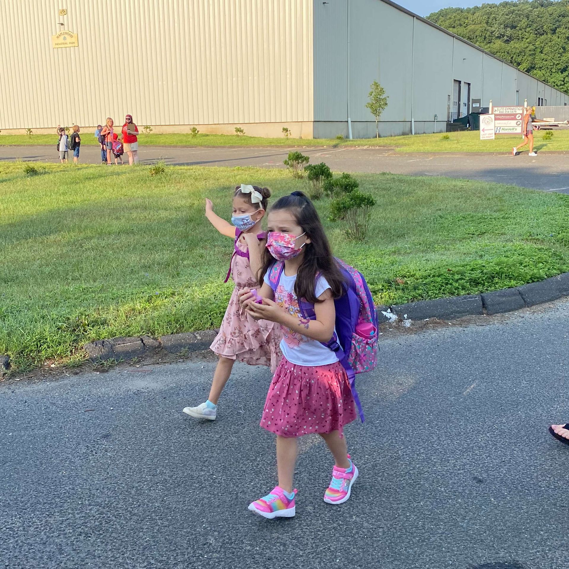 Two little girls wearing face masks are walking down the street.