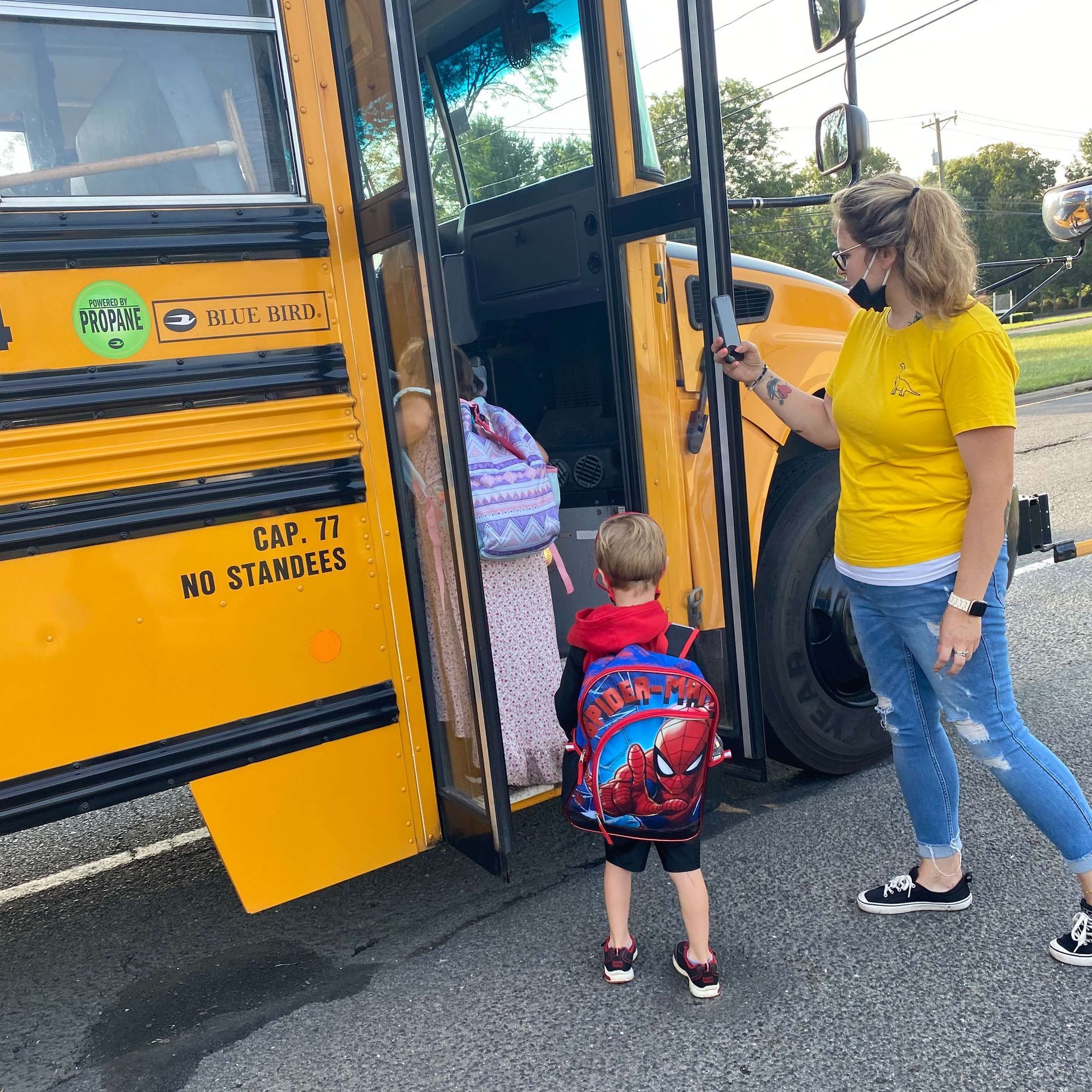A woman and child are getting on a yellow school bus.