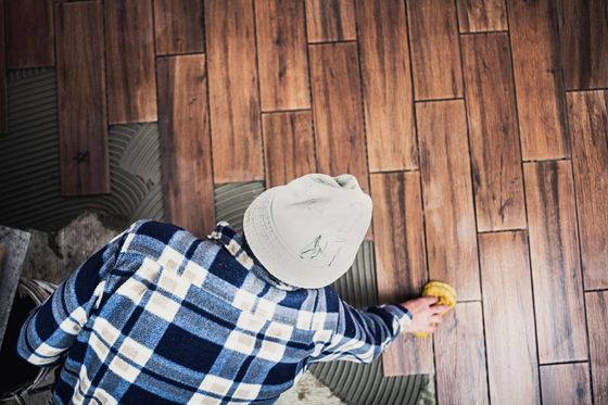 un uomo in una camicia a quadri pulisce un pavimento di legno con una spugna