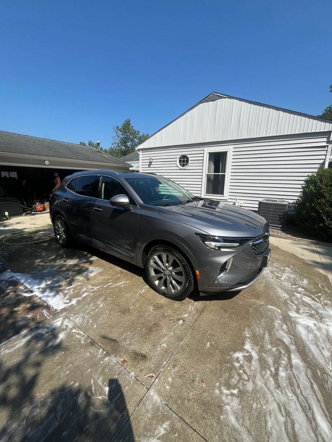 Gray SUV parked in a snowy driveway beside a white house under a clear blue sky