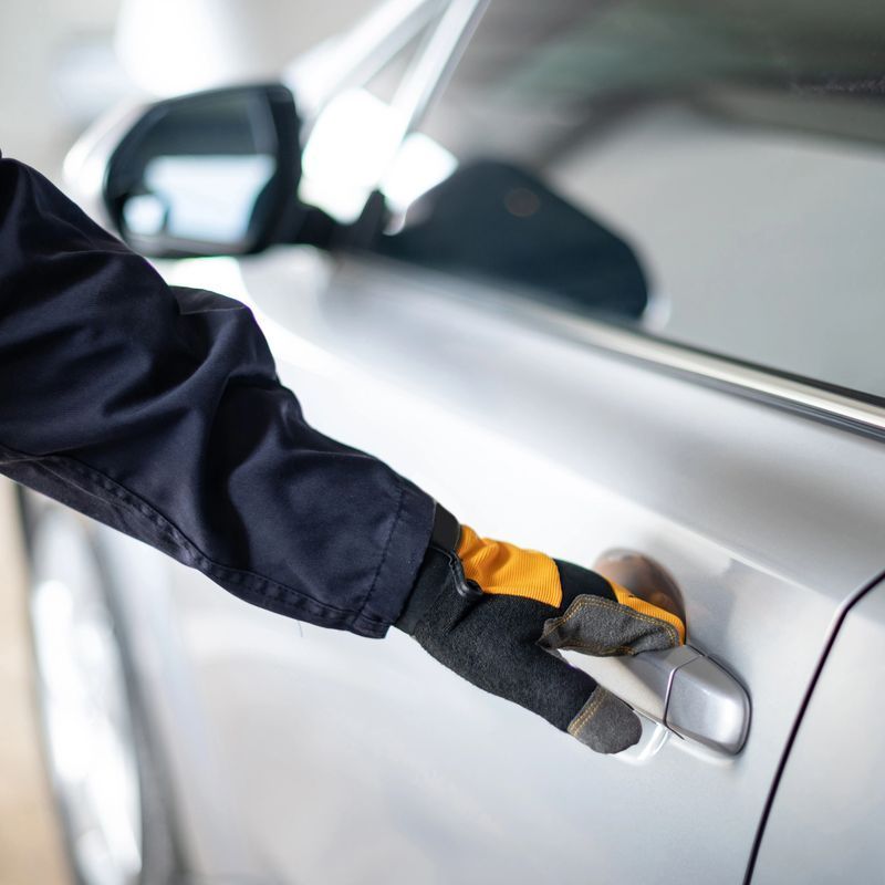 Gloved hand opening a silver car door handle