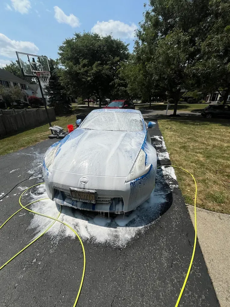 White car being washed with soap foam in a driveway on a sunny day