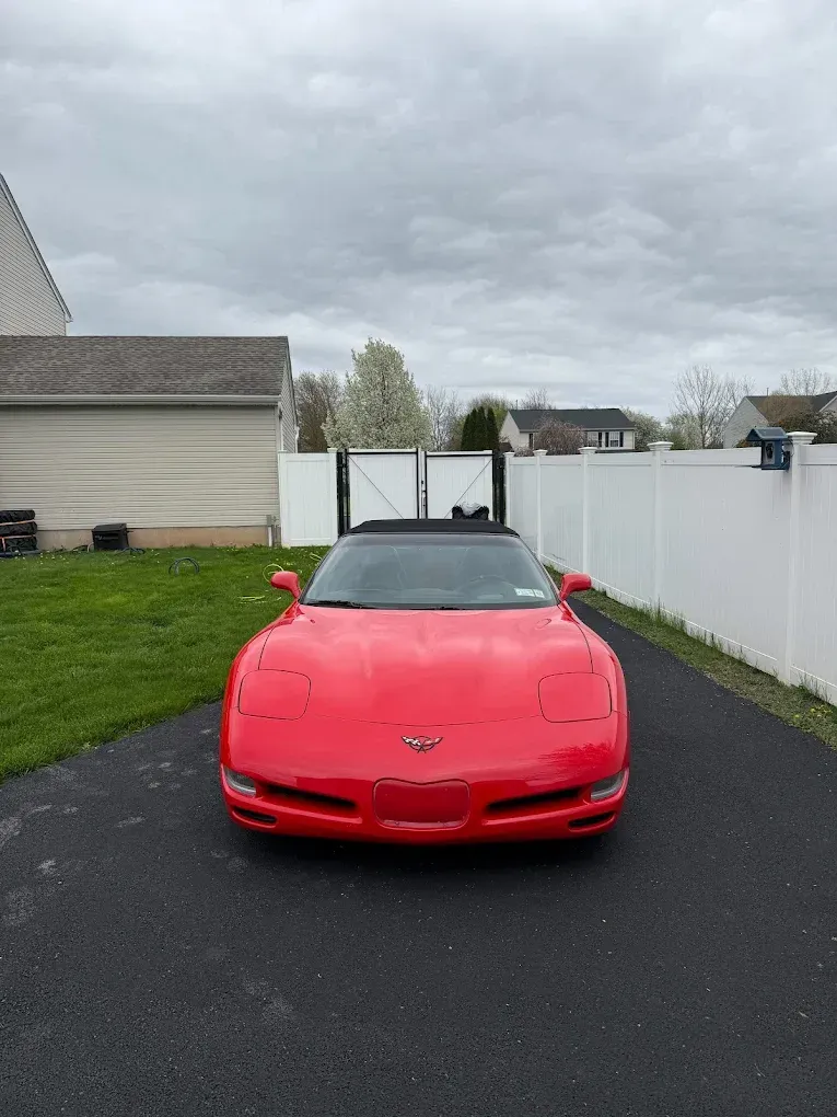 Red sports car parked on a driveway in front of a white fence and house.