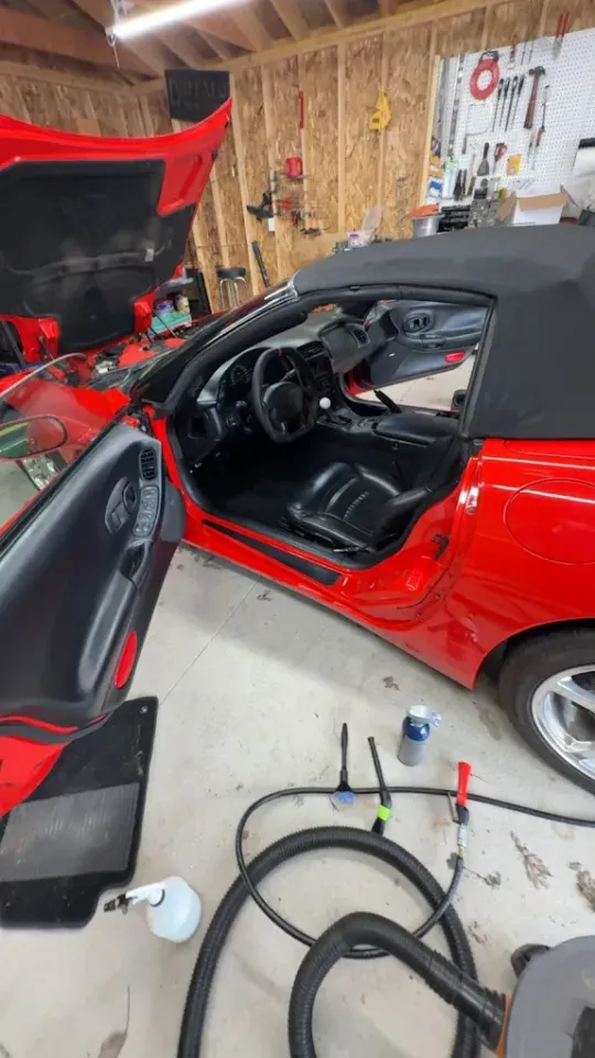 Red sports car with door open in a garage, showing the black interior and steering wheel.
