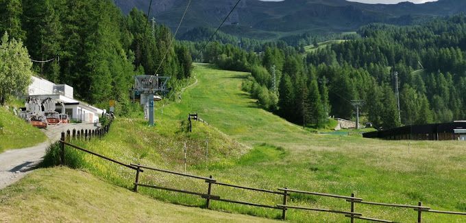 Una recinzione circonda un campo erboso con uno ski lift sullo sfondo.