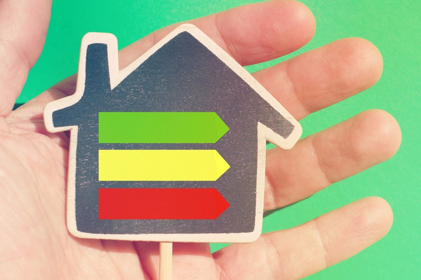 Una mano regge un cartello a forma di casa con frecce orizzontali verdi, gialle e rosse su sfondo verde.