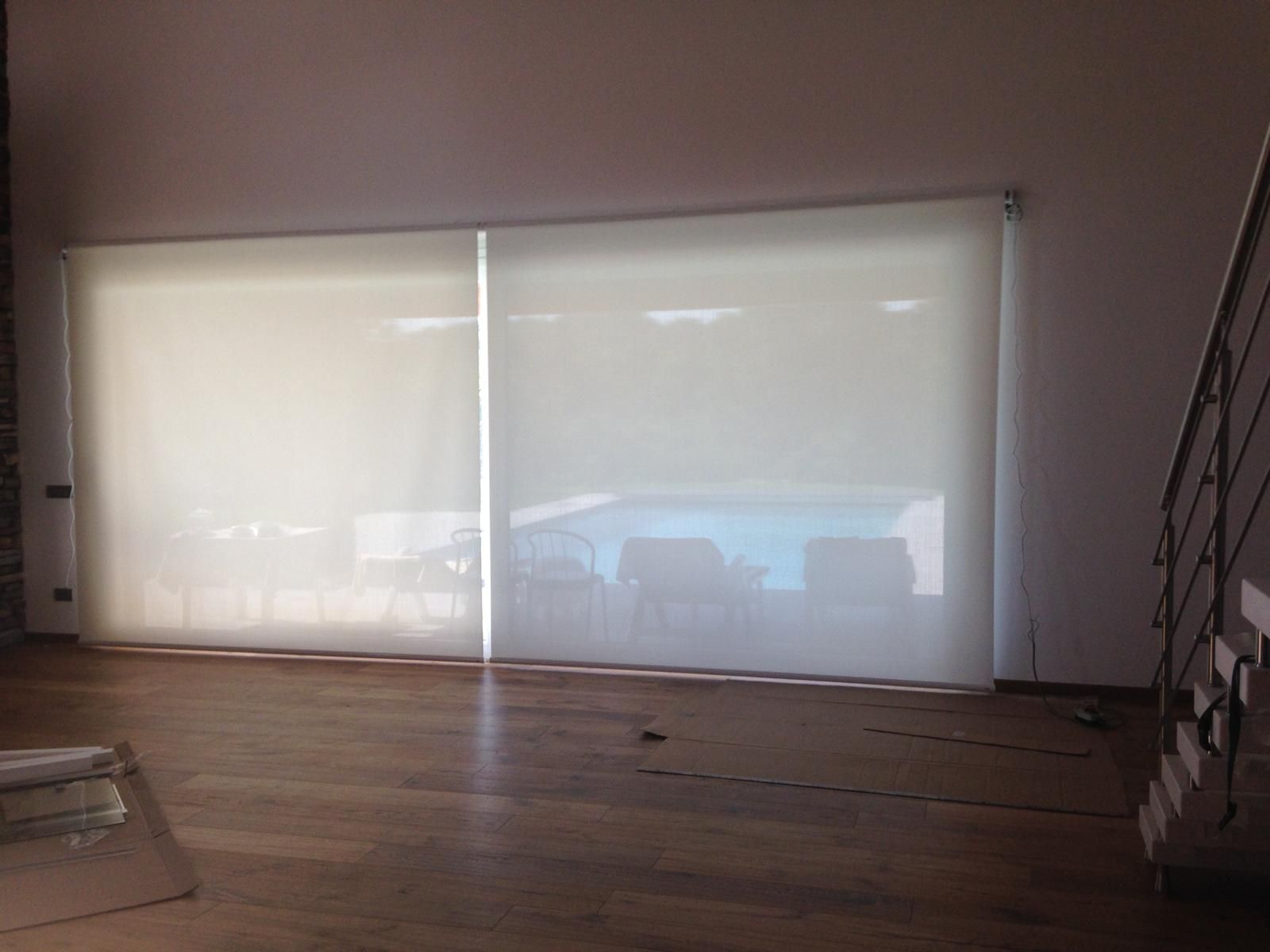 Le ampie finestre sono coperte da tende a rullo che vanno dal pavimento al soffitto, lasciando intravedere, in modo sfocato, il patio e la piscina sullo sfondo.