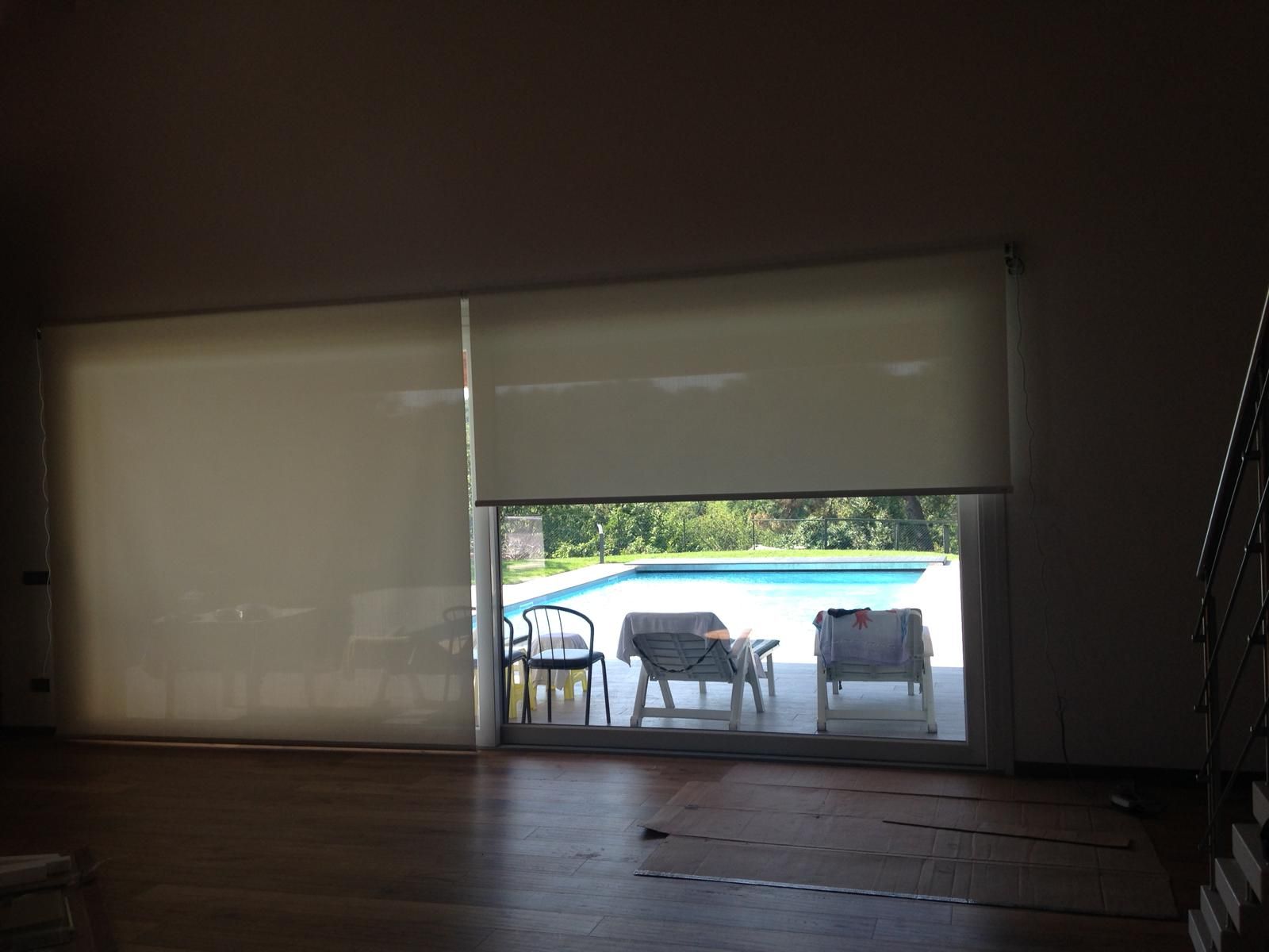 Ampie porte scorrevoli in vetro si affacciano su una piscina nel cortile sul retro, arredata con sedie da giardino e parzialmente coperta da tende a rullo.